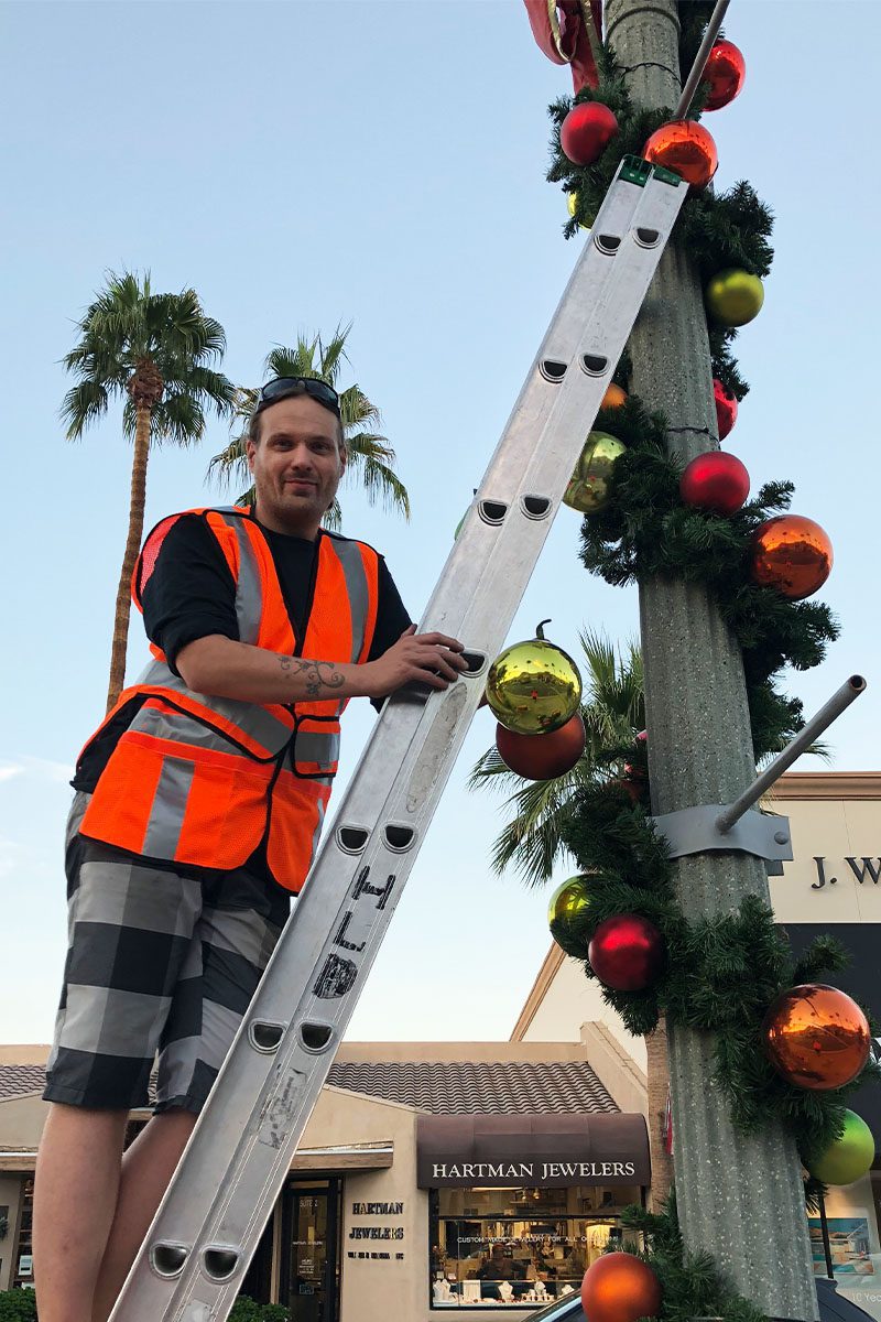 Very Christmas Inc employee installing Christmas garlands on El Paseo in Palm Desert